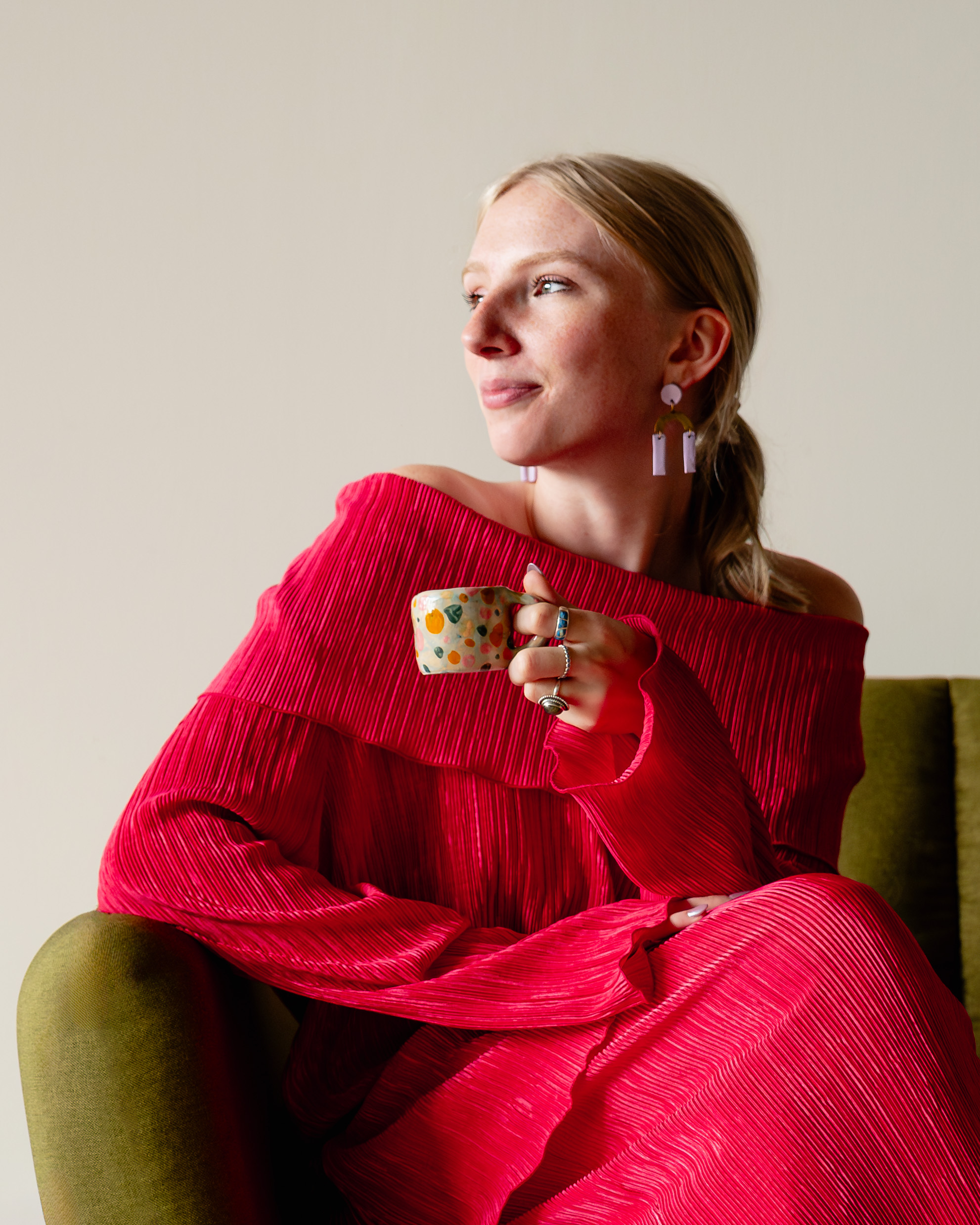 A young woman with a magenta, stylish top poses, coffee cup in hand